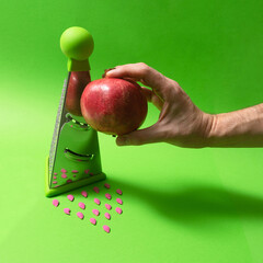 Pomegranate next to a grater with pumpkin seeds colored in red on the bottom. 45 degrees angle...