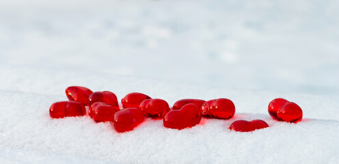 Closeup set of small bright red glass hearts on powdery snow of snowdrift at cold winter day, symbol of romantic love, St. Valentine's Day holiday concept, low angle shoot