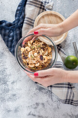 Woman hands showing an uncovered glass jar full of healthy granola over a rustic napkin next to a green lime.