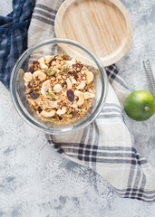 Overhead view of an uncovered glass jar full of healthy granola over a rustic napkin next to a green lime.