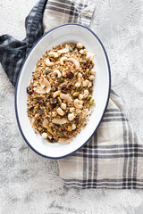 Metallic white tray full of delicious granola over a rustic napkin on a white and grey background.