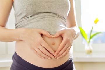 Portrait of young beautiful pregnant woman showing love heart with hands on stomach