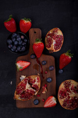 Strawberries, blueberries and pomegranates exposed on a wooden board in dark background.