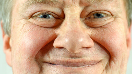 Front portrait of mature adult mans face which smiling.  Wrinkle skin and gray eye, looking at camera. Selective soft focus. Close-up.