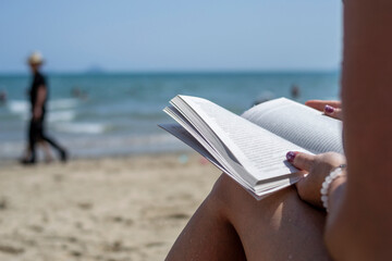 Woman reading a book on the beach, blurred background. Summer leisure on the beach