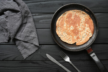 Hot pancake in black pan on black table with flour
