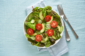 Vegan salad with tomatoes, cucumbers, avocado on pastel linen tablecloth. Vegeterian mediterranean food, low calories dieting meal