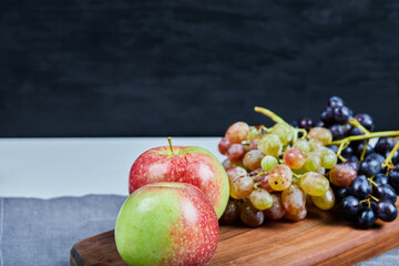 Apples with green and red grapes on a wooden board