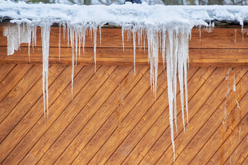 long icicles hang from the snow-covered roof against the wooden wall