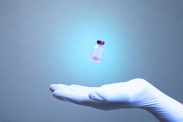 A palm in a latex medical glove over which a vaccine vial levitates in the air. Vaccinations against Covid-19. An injection against the virus
