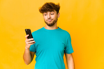 Young indian man holding a phone confused, feels doubtful and unsure.