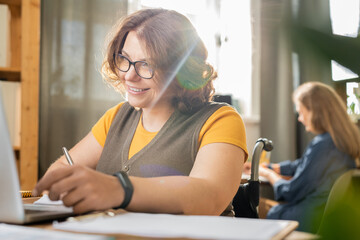 Young smiling disable office manager in casualwear looking at laptop display