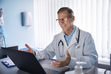 Happy old male doctor physician talking, consulting patient online by webcam video call on laptop computer. Telemedicine conference virtual tele meeting. E appointment, telehealth therapy concept. - obrazy, fototapety, plakaty