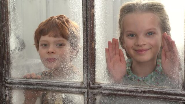 4K . Children, a red-haired boy and a girl with long hair in old clothes peek through a wooden window while creating Pinocchio in the carpenter's workshop of Geppetto carpenter Papa Carlo . Children's