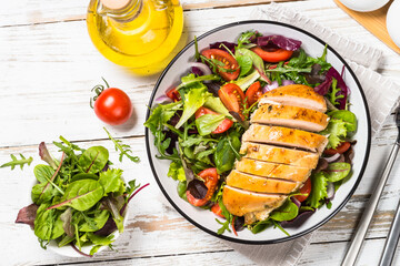 Green salad with baked chicken breast at white kitchen table. Healthy food, clean eating concept. Top view image.
