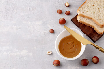 Traditional vegetarian breakfast close up. White bowl with natural hazelnut paste, toast sandwiches and nuts on a light background. Copy space.