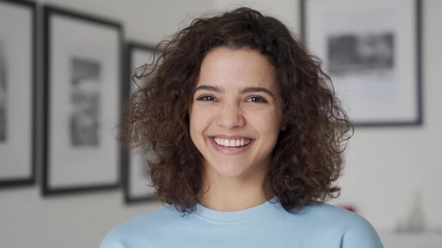 Cheerful happy cute young pretty hispanic latin woman looking at camera, laughing at home. Smiling positive 20s girl female model having fun feeling joy indoors, close up of laughing face, portrait.
