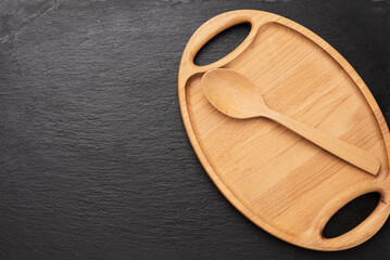 wooden spoon and empty oval brown wooden tray board on a black background,