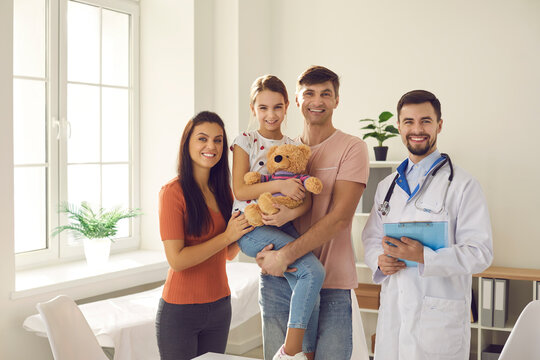 Portrait of happy mother, father and child together with family doctor. Mum, dad, little kid and friendly pediatrician or general practitioner standing in clinic office, smiling and looking at camera