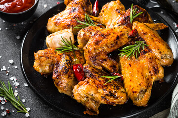 Grilled chicken wings with spices in black plate.