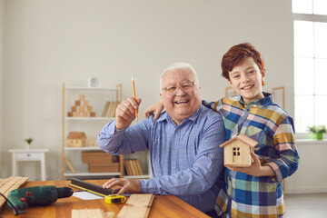Happy smiling senior elderly man grandfather and his positive grandson boy making measures for wooden birdhouse at home together. Happy family, hobby, grandfather and child concept
