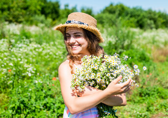 Happy kid smile in sun hat with chamomile flower bunch on sunny landscape vacation in countryside summertime, summer