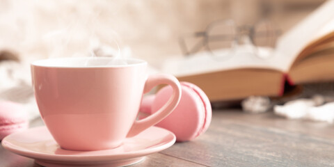 Cozy home composition. Book, plaid, steaming cup coffee or hot drink and macaroon on wooden table. Front view, copy space