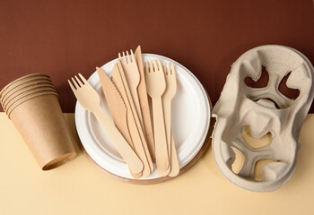 paper cup and wooden fork, empty round brown disposable plate made from recycled materials on a brown background