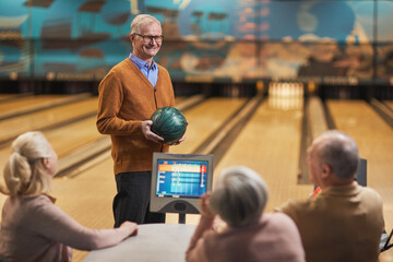 Portrait of happy senior man smiling at group of friends while playing bowling together at...