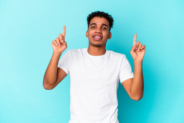 Young african american curly man isolated on blue indicates with both fore fingers up showing a...