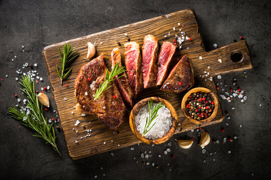 Beef steak. Grilled meat at wooden cutting board. Top view image at dark stone table.