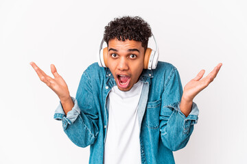 Fototapeta premium Young african american curly man isolated listening to music with headphones receiving a pleasant surprise, excited and raising hands.