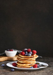 Delicious homemade pancakes in a plate with berries: raspberries, blueberries and maple syrup on a concrete background. With copy space.