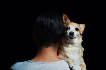 man in a white t-shirt hug his  old sad pet dog on shoulders isolated on black background, emotion of love and devotion between animal and owner