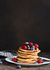 Delicious homemade pancakes in a plate with berries: raspberries, blueberries and maple syrup on a concrete background. With copy space.