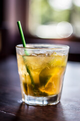 Caipirinha cocktail alcohol drink beverage with lemon slices ice straw and bokeh background on a wooden table