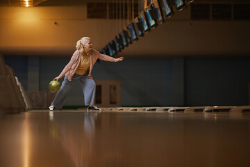 Wide angle side view at senior woman playing bowling alone while enjoying active entertainment at...