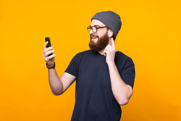 Photo of bearded hipster man looking at smartphone and listening music at earpods.