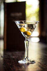Martini cocktail alcohol drink beverage with olives and bokeh background on a wooden table