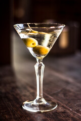 Martini cocktail alcohol drink beverage with olives and bokeh background on a wooden table
