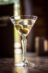 Martini cocktail alcohol drink beverage with olives and bokeh background on a wooden table