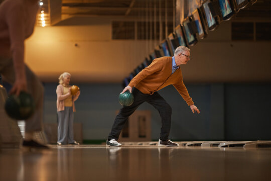 Wide Angle Side View At Senior People Playing Bowling While Enjoying Active Entertainment At Bowling Alley, Copy Space