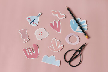 Paper cut abstract shapes, flowers and butterfly. Black old scissors and pencil on pink table background. Kids diy project, creativity and craft concept. Spring, summer design, flatlay, top view.
