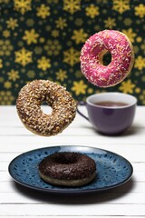 Donuts fall on a blue plate standing on a white wooden background.