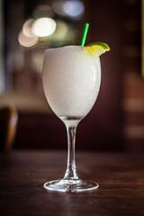 Frozen Passionfruit Vodka Slushy Daiquiri cocktail alcohol drink beverage with lemon, straw and bokeh background on a wooden table