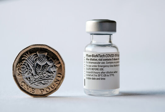 Genuine Pfizer BioNTech COVID-19 Vaccine vial, syringe and British one pound coin. Real vaccine photo. Selective focus. Stafford, United Kingdom - January 23 2021.
