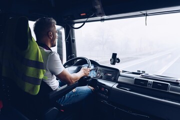 Handsome driver at the wheel of a truck at work. Work of a lorry driver. - obrazy, fototapety, plakaty
