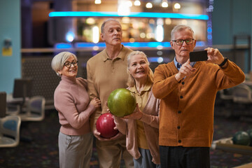 Group of senior people taking selfie photos playing bowling and enjoying active entertainment at bowling alley