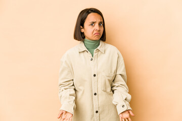 Young hispanic woman isolated shrugs shoulders and open eyes confused.