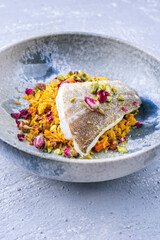 Modern style traditional sauteed skrei cod fish filet with skin in a bed of Persian jeweled saffron rice pilaw served in ceramic design bowl as close-up